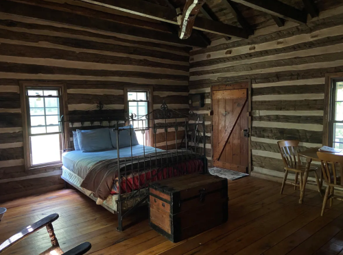 Cozy log cabin interior featuring a bed, wooden furniture, and a rustic door. Warm wooden floors and natural light.