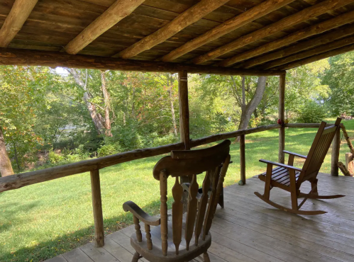 A rustic porch with two rocking chairs overlooking a green yard and trees in the background.