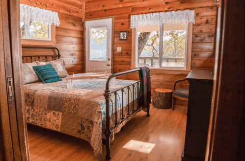 Cozy wooden bedroom with a quilted bed, large windows, and rustic decor, creating a warm, inviting atmosphere.