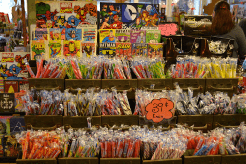 A colorful display of comic books and candy, featuring Marvel and DC characters, in a vibrant store setting.