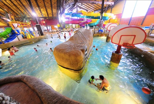 A vibrant indoor water park with slides, a rock feature, and families enjoying the pool area.