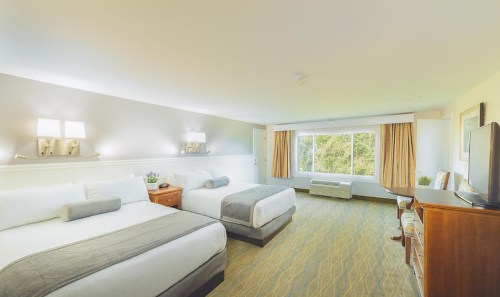 A spacious hotel room with two beds, a window with natural light, and a cozy seating area.