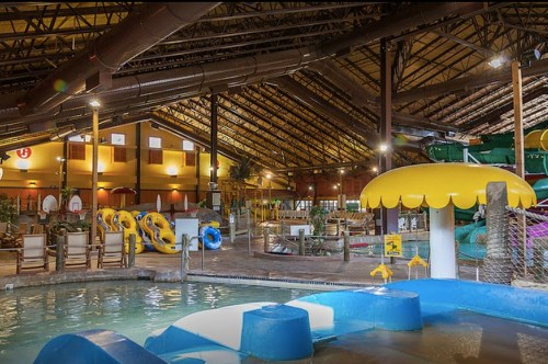 Indoor water park featuring slides, pools, and colorful inflatable tubes under a high ceiling with warm lighting.