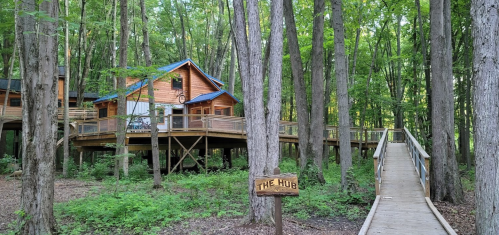 A wooden cabin surrounded by trees, with a walkway leading to a sign that reads "The Hub."