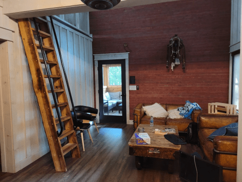 Cozy living room with wooden stairs, a brown couch, and a coffee table, featuring a rustic decor style.