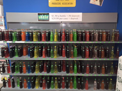 A display shelf filled with colorful bottles of soda, with pricing information above.