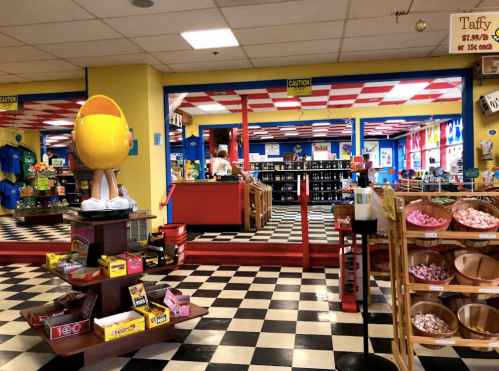 A colorful candy store interior with checkered floors, shelves of sweets, and a large yellow candy display.