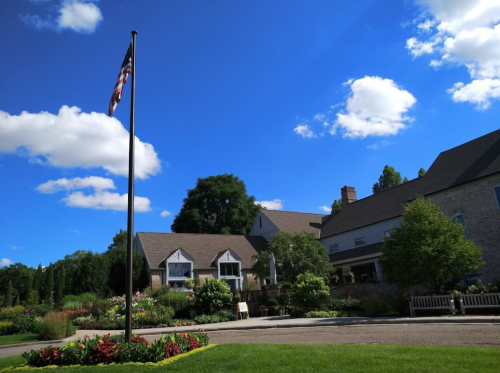 A scenic view of a building surrounded by colorful flowers and greenery, with a flagpole in the foreground under a blue sky.