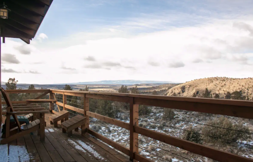 A wooden deck overlooks a snowy landscape with rolling hills and a cloudy sky in the distance.