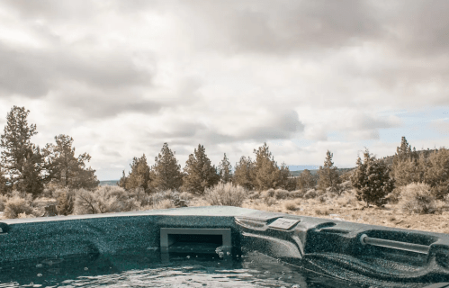 A hot tub overlooking a serene landscape of trees and cloudy skies.