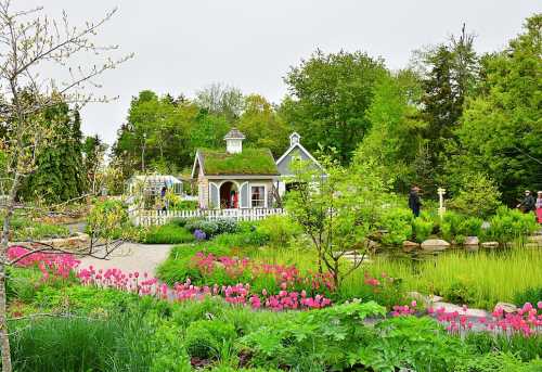 A vibrant garden with colorful flowers, a quaint cottage, and lush greenery under a cloudy sky.