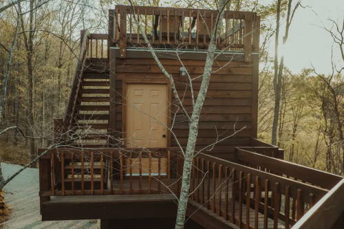 A wooden treehouse with a staircase and balcony, surrounded by trees in a serene outdoor setting.