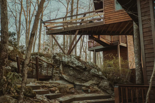 A wooden cabin perched on a rocky hillside, surrounded by bare trees and a winding stone pathway.