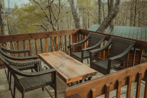 A cozy outdoor seating area with four wicker chairs and a wooden table, surrounded by trees.
