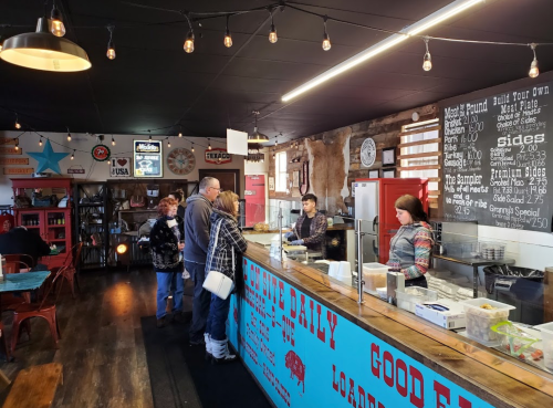 A busy restaurant counter with customers ordering food, colorful decor, and a menu displayed on the wall.