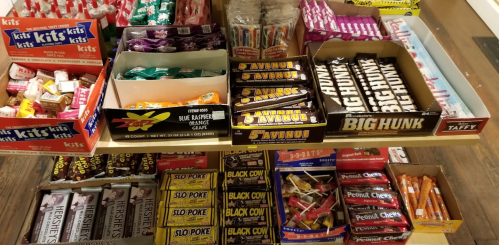 A display of various candy boxes and wrappers, including Slo Poke, Big Hunk, and Taffy, arranged on a wooden table.