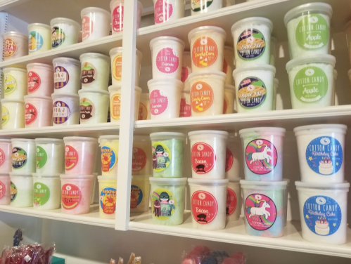 A colorful display of various cotton candy tubs on shelves, featuring unique flavors and vibrant labels.