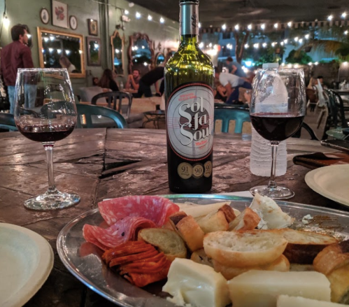 A table set with a bottle of wine, two glasses, and a platter of assorted meats and cheeses in a cozy, dimly lit setting.