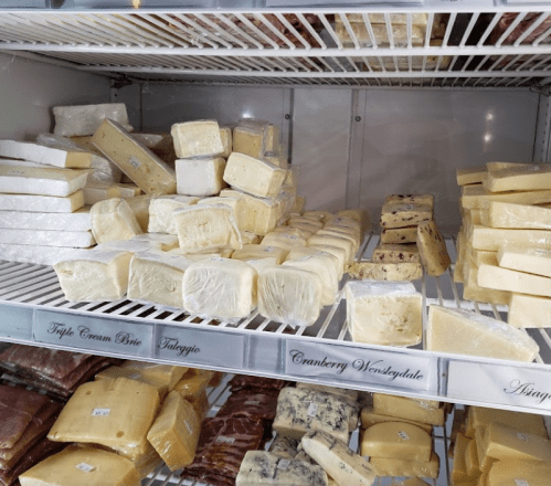 A display of various cheeses stacked on shelves, including blocks and wedges in different shapes and sizes.