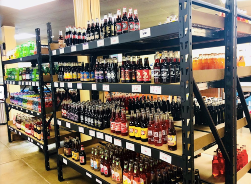 A store aisle filled with shelves of various colorful soda bottles and drinks.