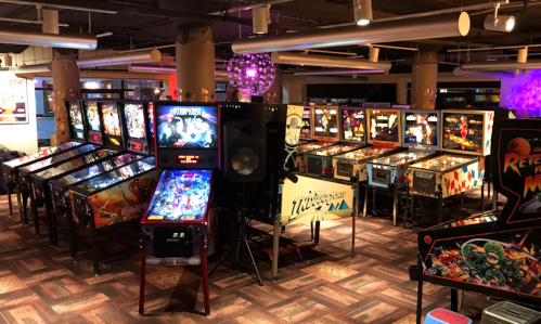 A vibrant arcade filled with various pinball machines, colorful lights, and a lively atmosphere.
