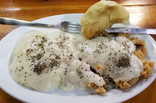 A plate of biscuits and gravy topped with black pepper, accompanied by a fork and knife on a wooden table.