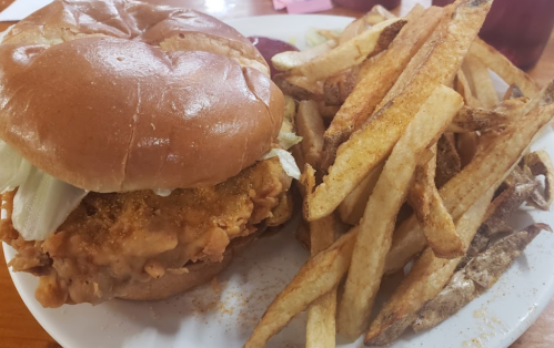 A crispy chicken sandwich with lettuce on a bun, served with a side of golden French fries on a white plate.