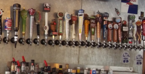 A wall-mounted bar tap system featuring various beer taps and labels in a lively setting.
