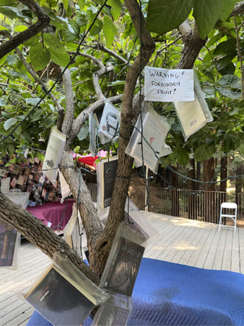 A tree with books hanging from its branches, accompanied by a sign that reads "WARNING! FORBIDDEN FRUIT!"