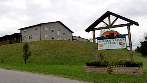 Sign for Walker Valley Market in front of a green hill and a two-story building under a cloudy sky.