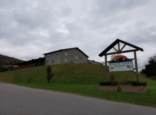 A sign for Walker Valley Market in front of a gray building on a grassy hill under a cloudy sky.