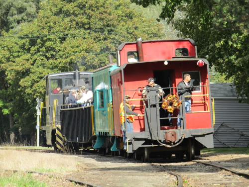 A colorful train with a red caboose and green car, passengers enjoying a ride on a sunny day.