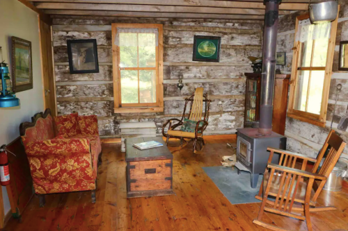 Cozy interior of a rustic cabin featuring wooden walls, a stove, and vintage furniture including a rocking chair.