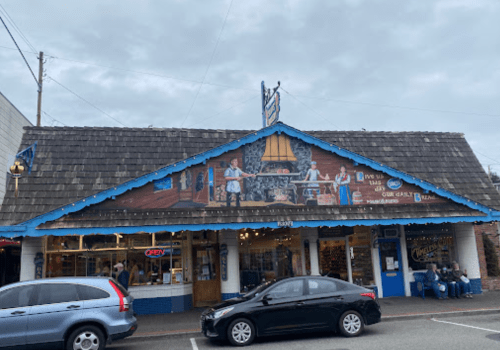A colorful storefront with a mural, featuring a blue roof and "Open" sign, with cars parked in front.