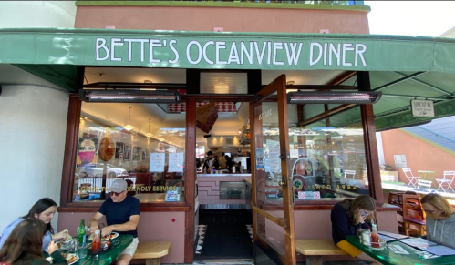 Exterior of Bette's Oceanview Diner, featuring a green awning and patrons dining outside. Bright and inviting atmosphere.