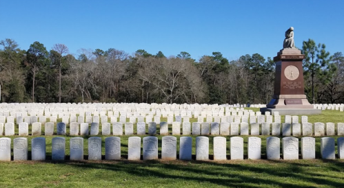 A cemetery with rows of white gravestones and a large monument surrounded by trees.