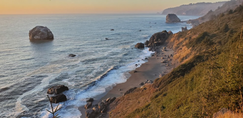 A serene coastal landscape at sunset, featuring rocky shores, gentle waves, and a misty horizon.