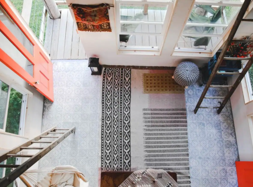 Aerial view of a cozy room with patterned rugs, a wooden ladder, and large windows letting in natural light.