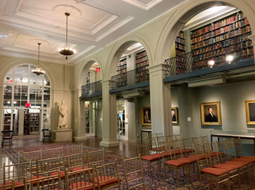 A spacious library interior with tall bookshelves, elegant arches, and rows of chairs set up for an event.