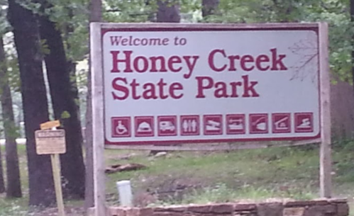 Sign welcoming visitors to Honey Creek State Park, featuring icons for amenities and activities available.