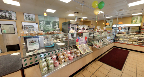 A colorful bakery display filled with various pastries, cakes, and candies, with balloons and decorations in the background.