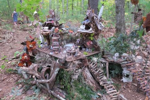A whimsical fairy house made of natural materials, nestled in a forest with trees and foliage surrounding it.