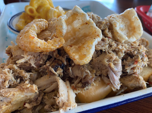 A plate of shredded meat topped with crispy pork rinds, served with a side of macaroni and cheese.