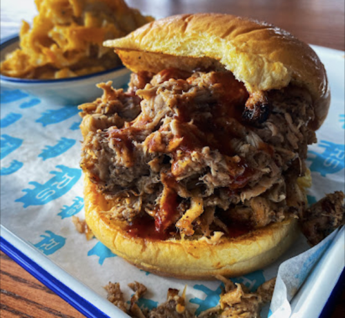 A close-up of a pulled pork sandwich with barbecue sauce on a soft bun, served with a side of macaroni and cheese.
