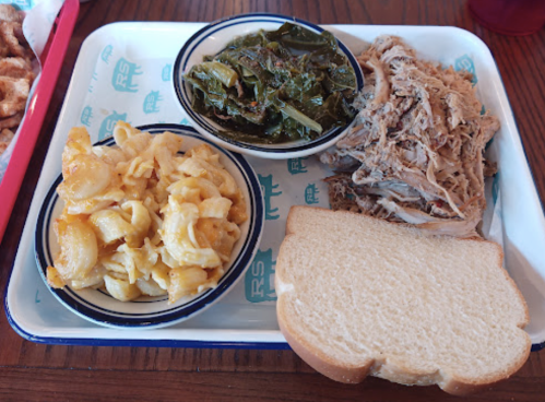 A tray with pulled pork, collard greens, macaroni and cheese, and a slice of white bread.