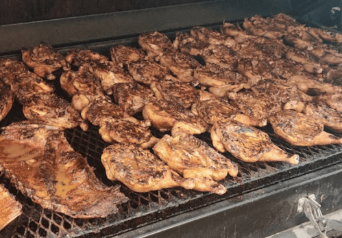 Grilled chicken pieces cooking on a barbecue grill, with a smoky, charred appearance.