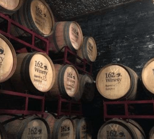 A stack of wooden wine barrels labeled "162 Winery" in a dimly lit cellar.