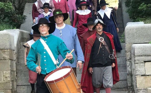 A group of people in historical costumes, including a drummer, walking down stone steps.