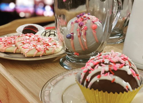 A wooden tray with decorated cookies and chocolate treats, featuring colorful sprinkles and icing.