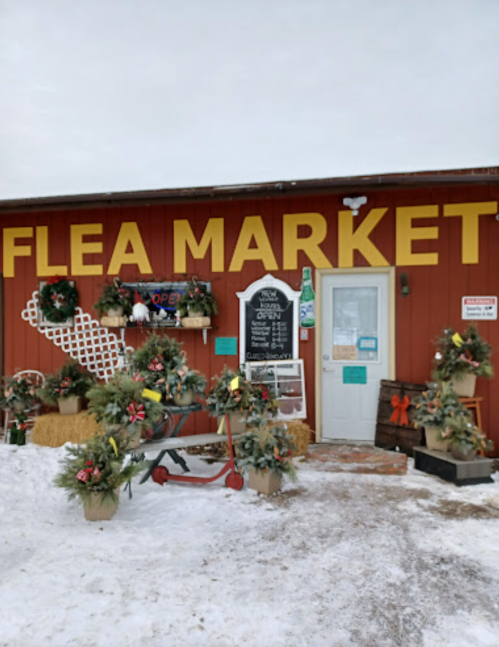 A red building with "Flea Market" sign, decorated with wreaths and snow, featuring a door and a chalkboard menu.